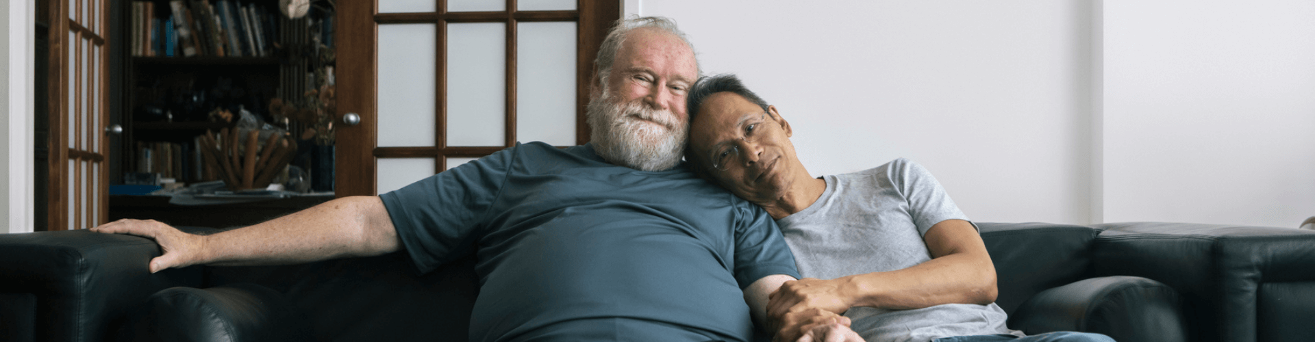 Two older people embrace on a sofa in a living room